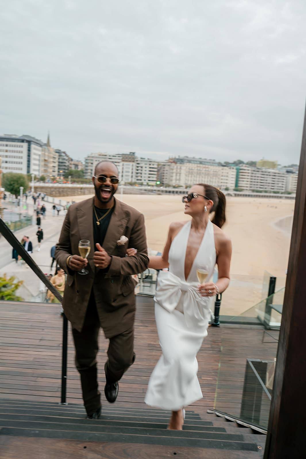 Una pareja riendo con copas de champán en las escaleras sobre la playa de La Concha, San Sebastián